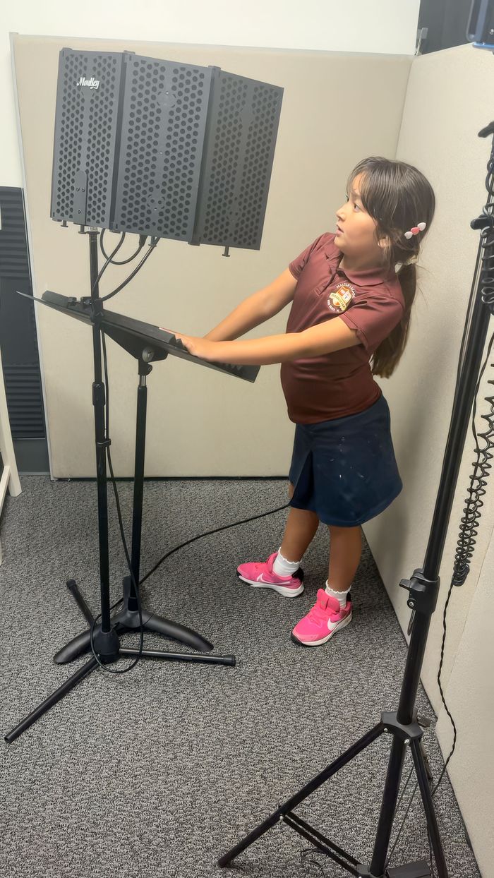 A child voice actor recording lines at a microphone stand in a sound booth for Cosmic Cubs